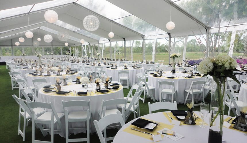 An image from within a setup clear span tent of dozens of round tables with 10+ chairs per table in a tent with no tent polls inside and transparent panels in the ceiling of the tent to allow natural light in, spacious and beautiful for an event.